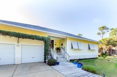 a yellow house with two garages and stairs leading up to the front door on a sunny day