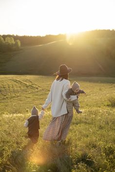 a woman in a hat and dress walking through a field with two small children holding hands