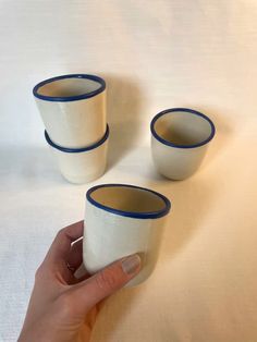 three white cups with blue rims are being held by a woman's hand