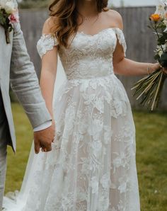 a bride and groom hold hands as they walk through the grass