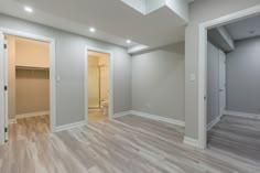 an empty room with white walls and wood flooring is pictured in this image, there are two doors leading to the bathroom