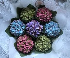 there are many different colored flowers in the box on the lace doily tablecloth