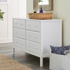 a white dresser with baskets on top of it next to a mirror and rug in a room