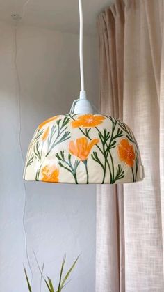 an orange and white flowered lamp hanging from a light fixture in a room with curtains