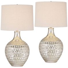 two clear glass lamps with white shades on each one and a beige shade on the other