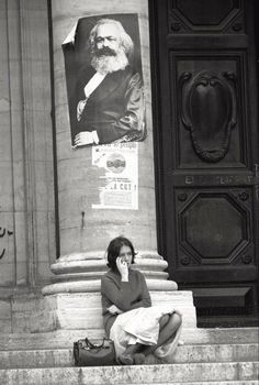 a woman sitting on the ground talking on her cell phone in front of a building