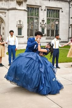 a woman in a blue dress is kneeling down on the ground with other people standing around her