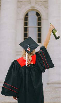 a woman in graduation cap and gown holding up a bottle of wine to the side