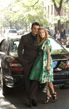 a man and woman standing next to each other in front of a car