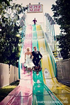 a bride and groom are sitting on a colorful slide at a wedding reception in an amusement park