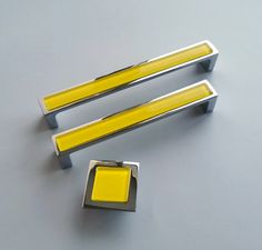 two yellow and silver handles on a gray surface, one has a square button in the middle