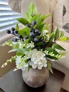 a vase filled with white and blue flowers on top of a table next to a couch