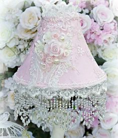 a pink lamp shade sitting on top of a table next to white roses and other flowers