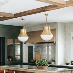 a kitchen with green cabinets and white marble counter tops, two pendant lights over the island