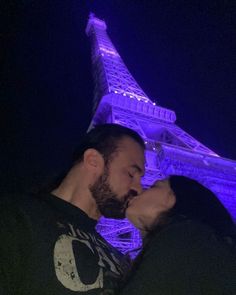 a man and woman kissing in front of the eiffel tower with purple lights