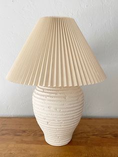 a white lamp sitting on top of a wooden table next to a wall and floor