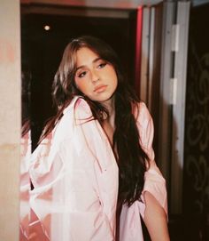 a woman standing in front of a door wearing a pink shirt and black pants with long hair