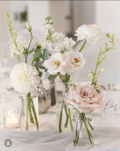 two vases with flowers are sitting on a table next to candles and glass jars