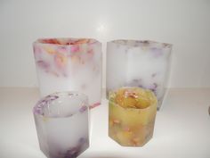 three different colored vases sitting next to each other on a white counter top, one is filled with liquid and the other has fruit in it's bottom