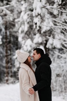 a man and woman standing next to each other in front of snow covered trees on a snowy day