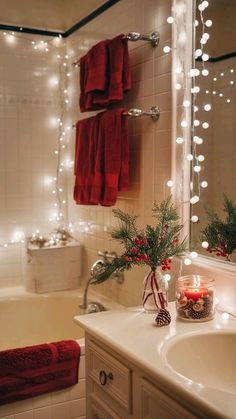 a bathroom decorated for christmas with lights on the shower curtain and red towels hanging over the bathtub