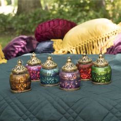 four colorful glass jars sitting on top of a blue table cloth next to some pillows