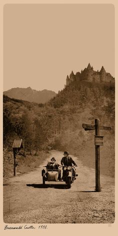 an old photo of two people on a motorcycle driving down the road in front of a cross