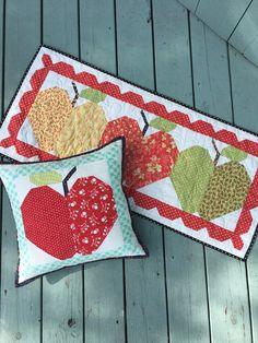 two pillows with apples on them sitting next to each other in front of a wooden deck