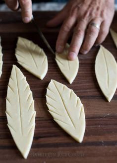 a person cutting up leaves with a knife on top of a wooden table in front of them