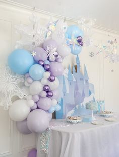 a table topped with balloons and snowflakes next to a castle covered in frosting