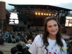 a woman standing in front of a crowd at a music festival wearing a white t - shirt