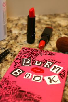 a red book with the words burn on it next to lipstick and makeup brushes sitting on a counter