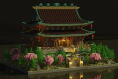 a model of a chinese building with flowers and trees around it, in front of a body of water