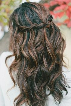 the back of a woman's head with long wavy brown hair and flowers in the background