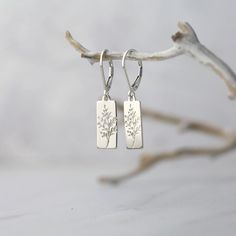 "Dainty, tiny silver hand stamped botanical rectangular tag earrings, paired with secure lever-back earwires. Hand stamped with a minimalist wildflower design, these petite dangle leverback earrings are a customer favorite because they are so lightweight and easy to wear! All in nickel-free solid sterling silver metal for long lasting quality. * Overall earring length is about 1.3 inches. * Tag dangles are about 0.67 inch by 0.27 inch. * All components are nickel-free sterling silver. * Sterling Nickel Free Rectangular Pendant Earrings As Gift, Nickel-free Rectangular Pendant Earrings As Gift, Everyday Rectangular Nickel Free Earrings, Everyday Rectangular Nickel-free Earrings, Everyday Nickel-free Rectangular Earrings, Minimalist Sterling Silver Earrings With Birth Flower, Minimalist Sterling Silver Birth Flower Earrings, Personalized Minimalist Silver Earrings, Personalized Sterling Silver Earrings For Everyday