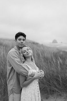 a man and woman hugging in front of tall grass on the beach with ocean behind them