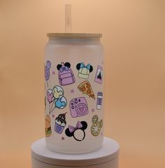 a glass jar with mickey mouse and other items painted on the lid, sitting on a stand