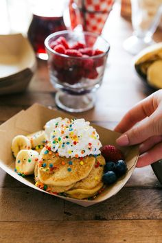 a person is reaching for some fruit on top of pancakes with whipped cream and sprinkles