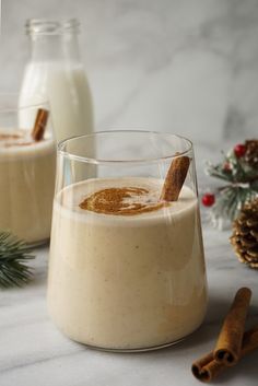 two glasses filled with mexican coquito on top of a white table next to cinnamon sticks