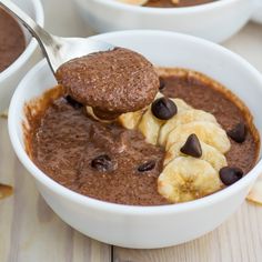 a spoon full of chocolate pudding with bananas and chocolate chips on the side in two white bowls