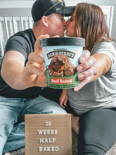 a man and woman sitting on the floor kissing while holding up a cup of ice cream