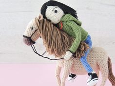 a crocheted doll riding on the back of a toy horse with long hair