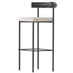 a black and white bar stool with a cushion on the backrest, in front of a gray background