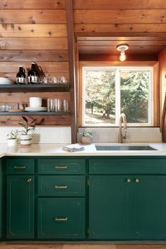 a kitchen with green cabinetry and wooden walls, along with open shelving above the sink