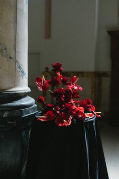 red flowers are sitting on top of a black table cloth in front of a pillar