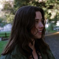 a woman with long hair standing in front of a tree and looking off into the distance