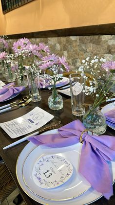 the table is set with purple and white flowers in vases, napkins, and silverware