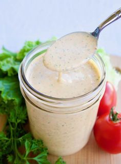 a spoon full of dressing sitting on top of a cutting board next to tomatoes and lettuce