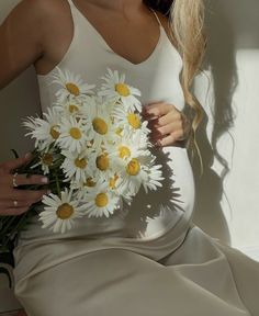 a pregnant woman holding a bouquet of daisies