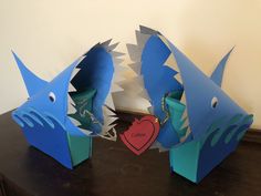 two paper sculptures of shark heads with a heart in the mouth, on a table